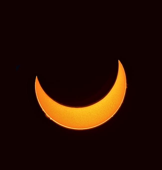 Golden crescent sun during eclipse (through a filter), with little flares along the edge.