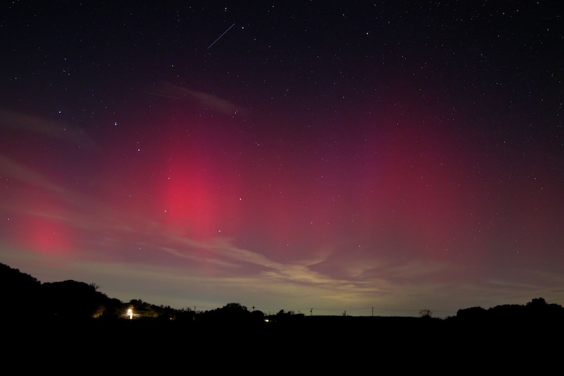 Vast vertical curtains of red light in the dark sky above a dimly glowing horizon.