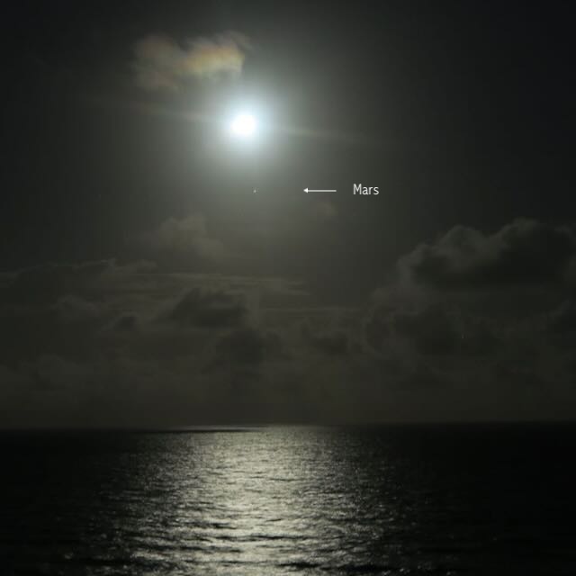 Black-and-white photo of bright fuzzy-looking moon, with a dot of light below it (Mars, labeled), rising over the ocean.