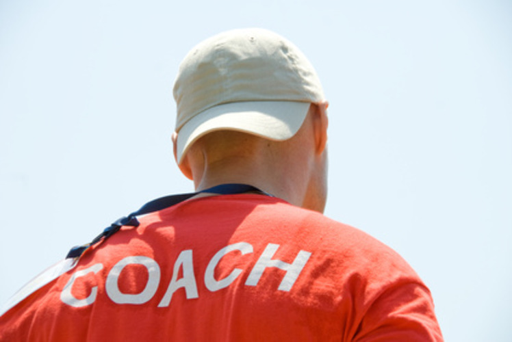 A person wearing a red back-printed school coach T-shirt