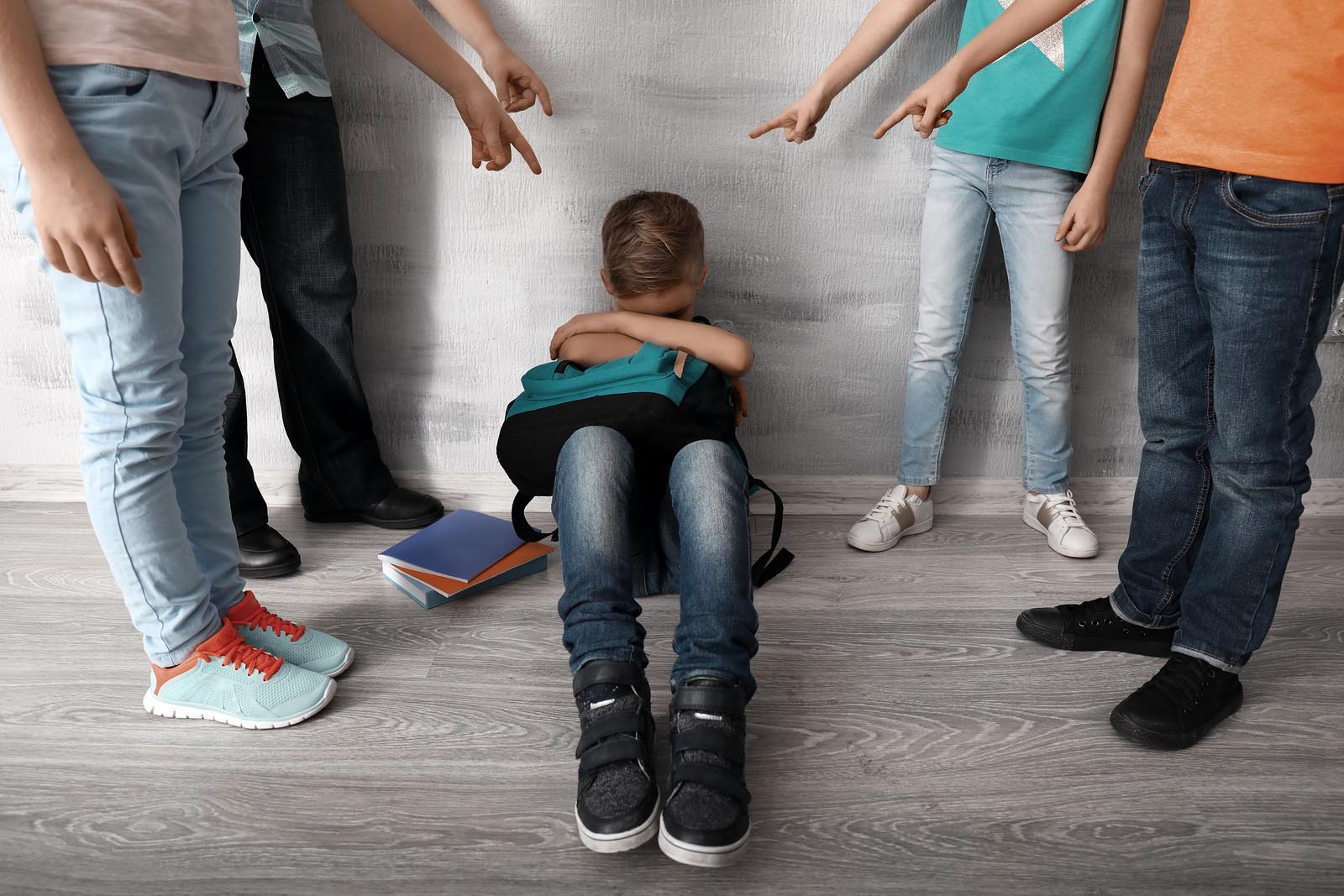 Four children bullying and harassing a sad boy sitting curled up on the floor