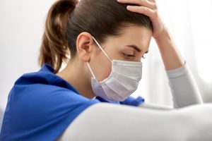 A young female doctor or nurse wearing face protective mask for protection from virus disease sitting on floor and holding to head