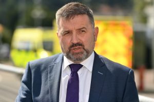 Northern Ireland health minister Robin Swann pictured in a suit with ambulances in the background