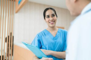 Nurse in blue uniform holding blue clipboard speaking to a doctor in a white uniform on a hospital ward