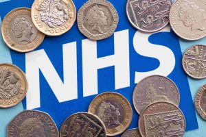 Picture of different British coins on top of a sign which has the NHS logo