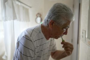 Image of an older man brushing his teeth in the mirror.