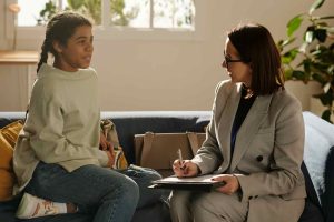 Image of social worker / public health nurse sat on a sofa talking to a child.