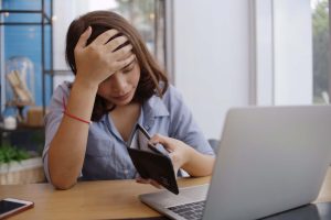 Stock image of nursing student looking stressed. She is sat at a laptop looking at an empty purse.