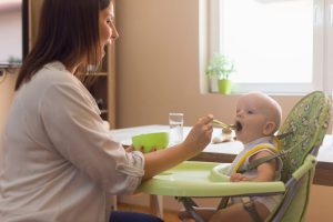 Stock image of mother feeding a baby in a high chair.