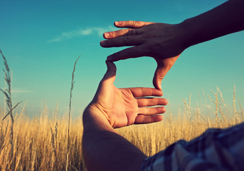 two hands make the shape of a rectangle to frame a view of blue skies and beautiful fields