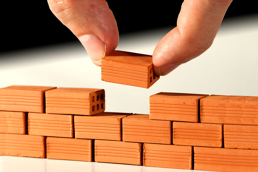 a person places miniature bricks in a wall