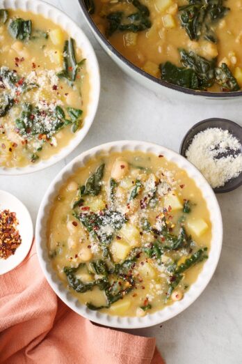 Two bowls of kale and bean soup garnished with grated parmesan with soup pot nearby.