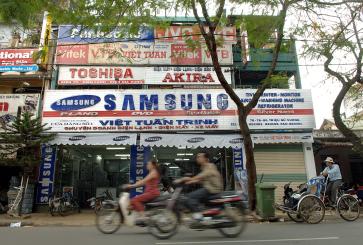 People on motorcycles ride past a Samsung store in Vietnam.