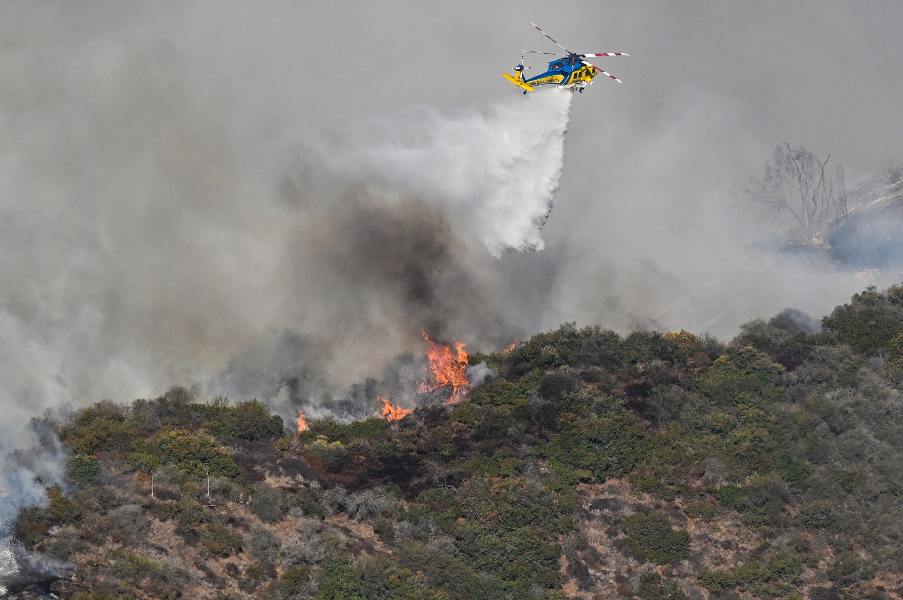 Helicopters battle flames as Palisades Fire burns on the Santa Monica Mountains on January 11, 2025 in Brentwood, California.