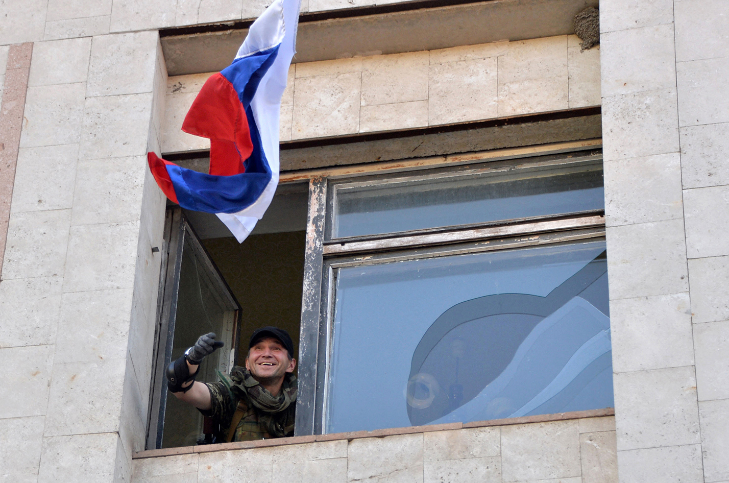 A Ukrainian soldier smiles as he throws a Russian flag out of the window of a building.