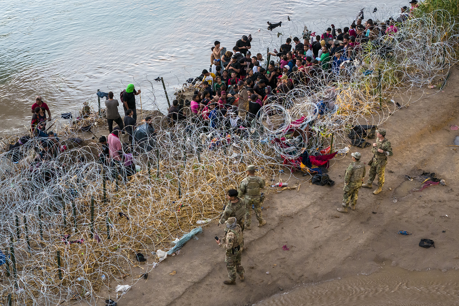 Texas National Guard troops wait on the side of the river as asylum-seeking migrants cross the Rio Grande.