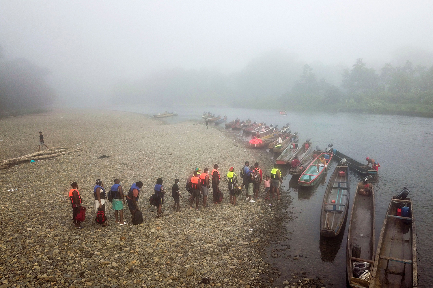 Migrants queue for rowboats on the bank of a river in the fog.