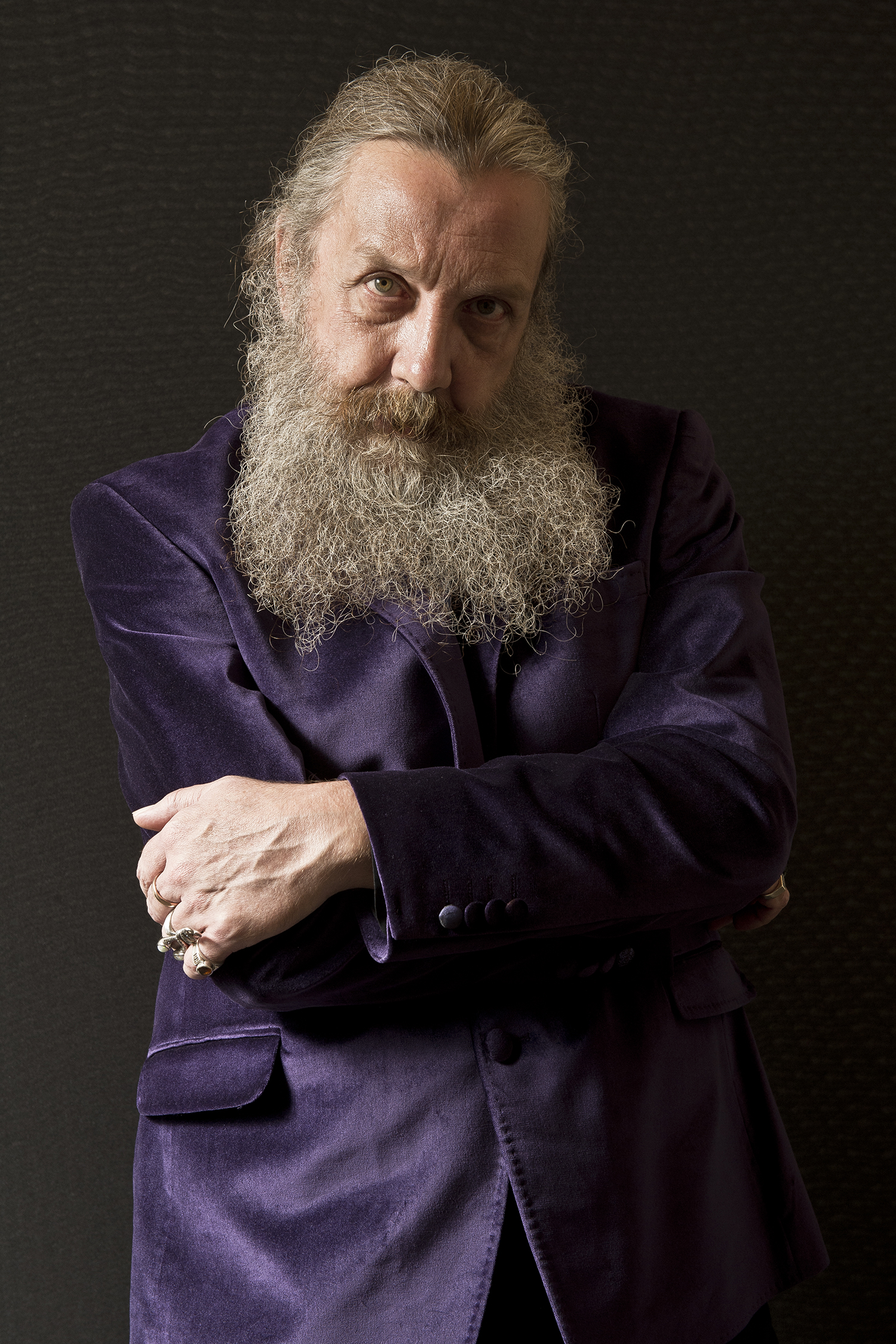 Alan Moore poses for a portrait in a purple suit.