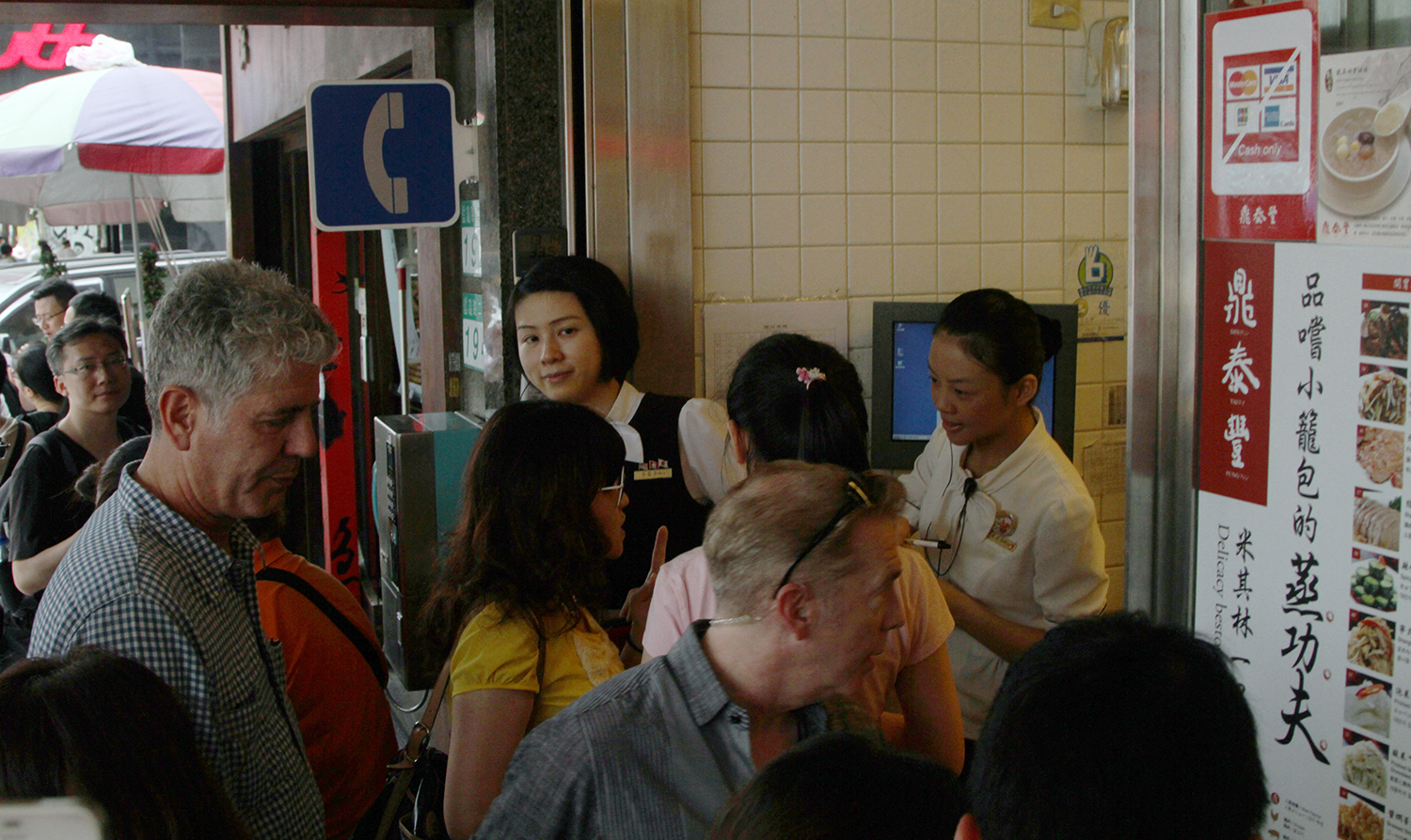 Anthony Bourdain is seen among a group of patrons outside a restaurant with signs in Chinese characters.