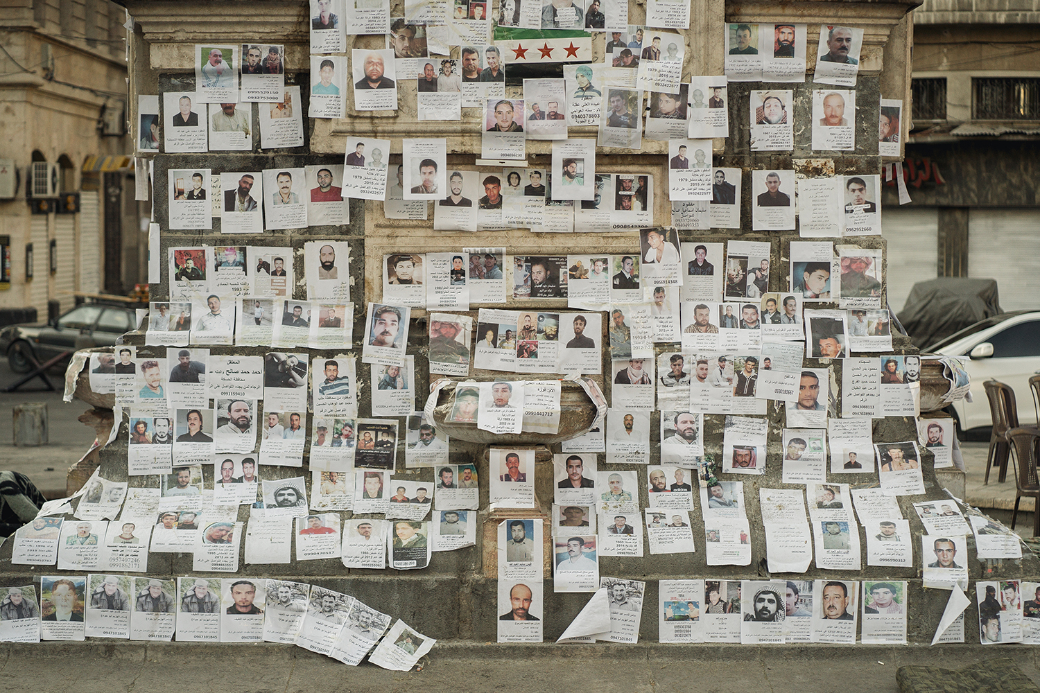 The stone surface of what looks like an outdoor monument is filled with multiple rows of fliers showing missing people. There are about a hundred flyers overall.