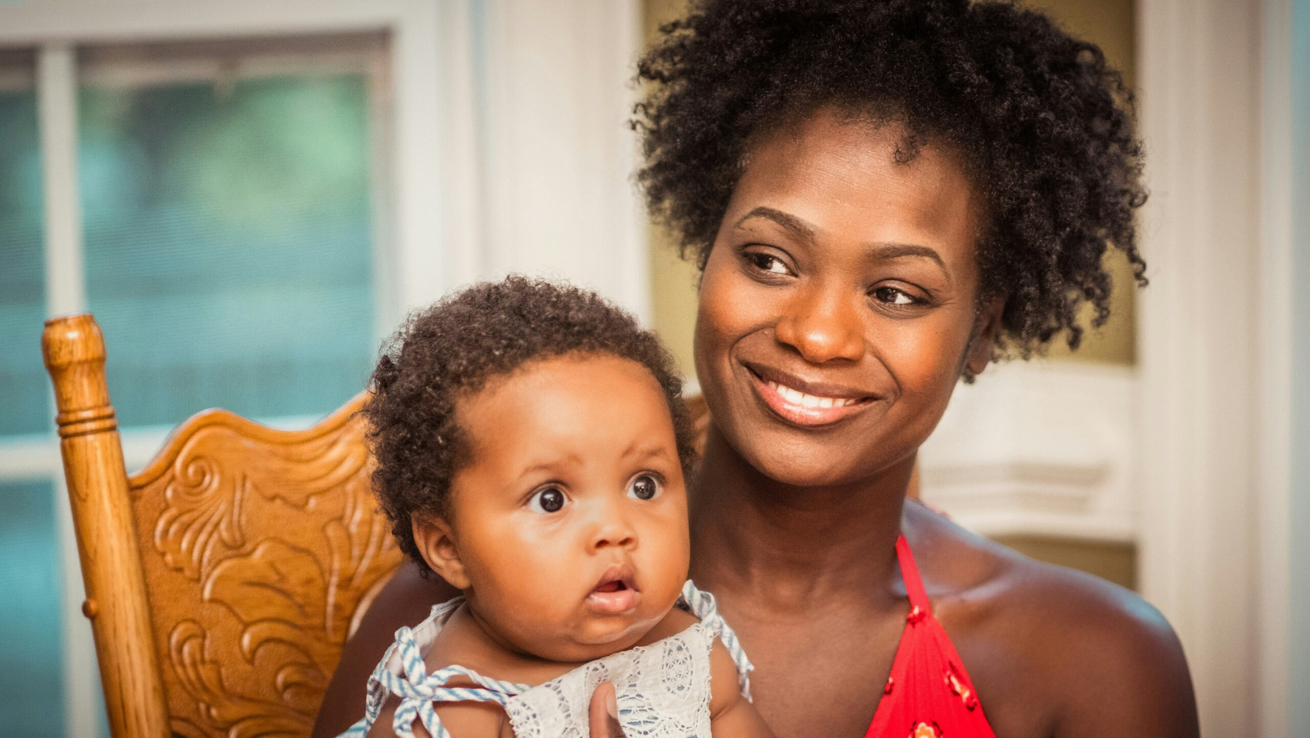 A mother sits smiling with her infant child in a rocking chair