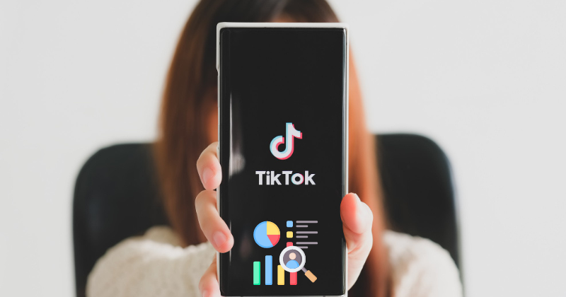 A woman holding up a phone with the tiktok logo on it.