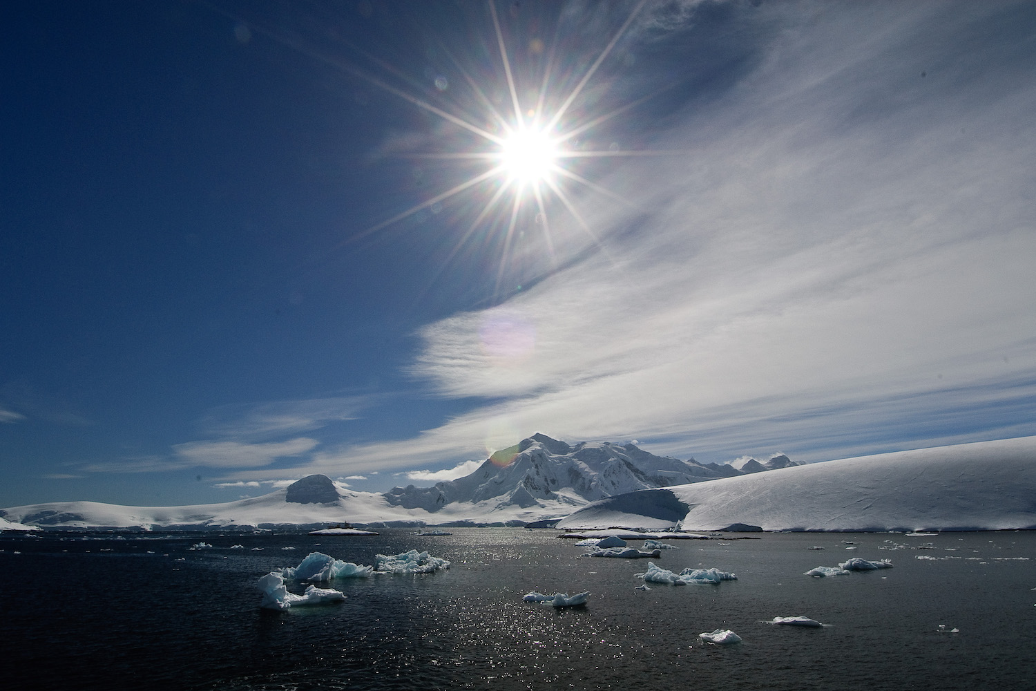 Image of the sun shining over snow and water in Antarctica.