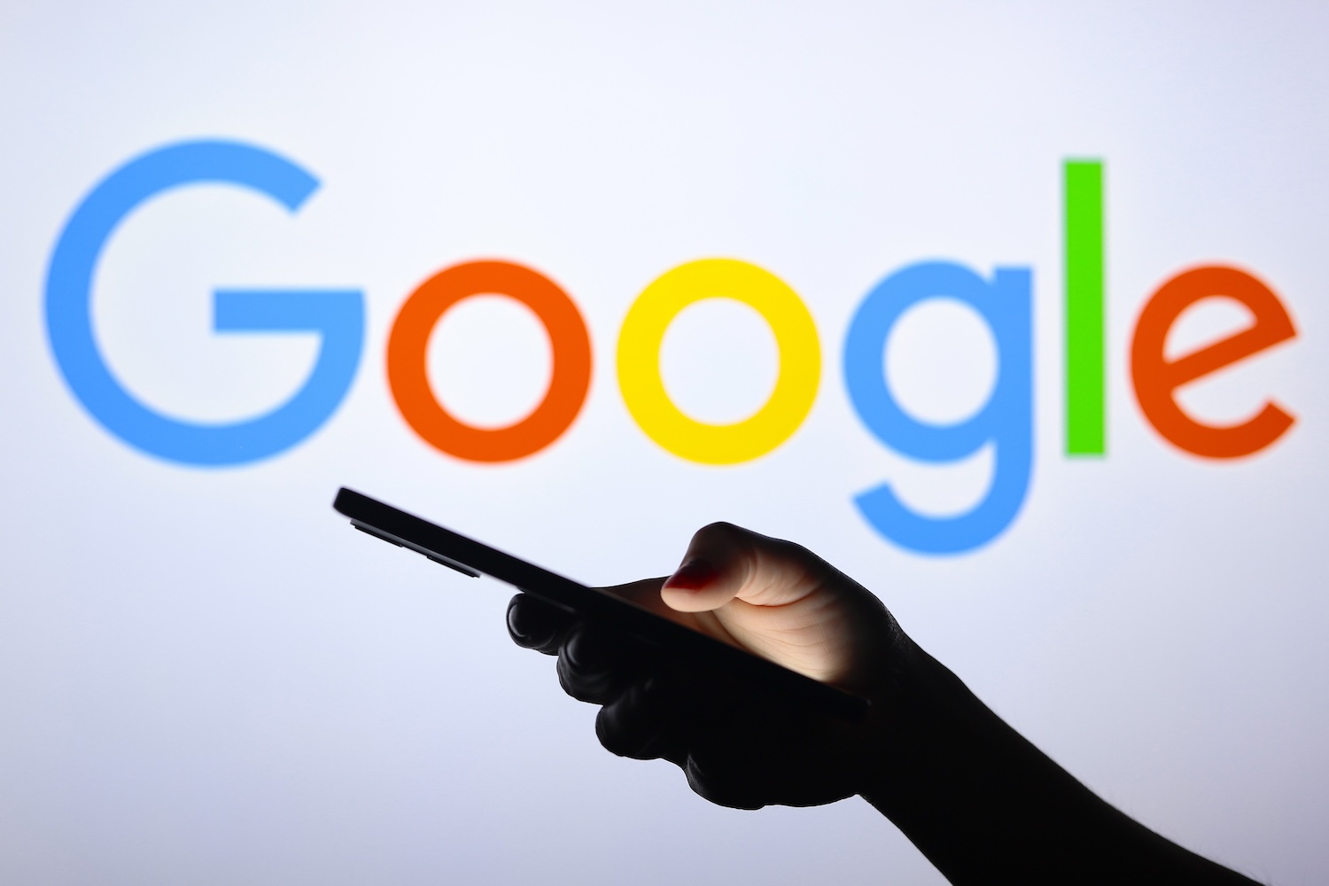 Google's logo is shown behind a silhouette hand holding a smartphone.