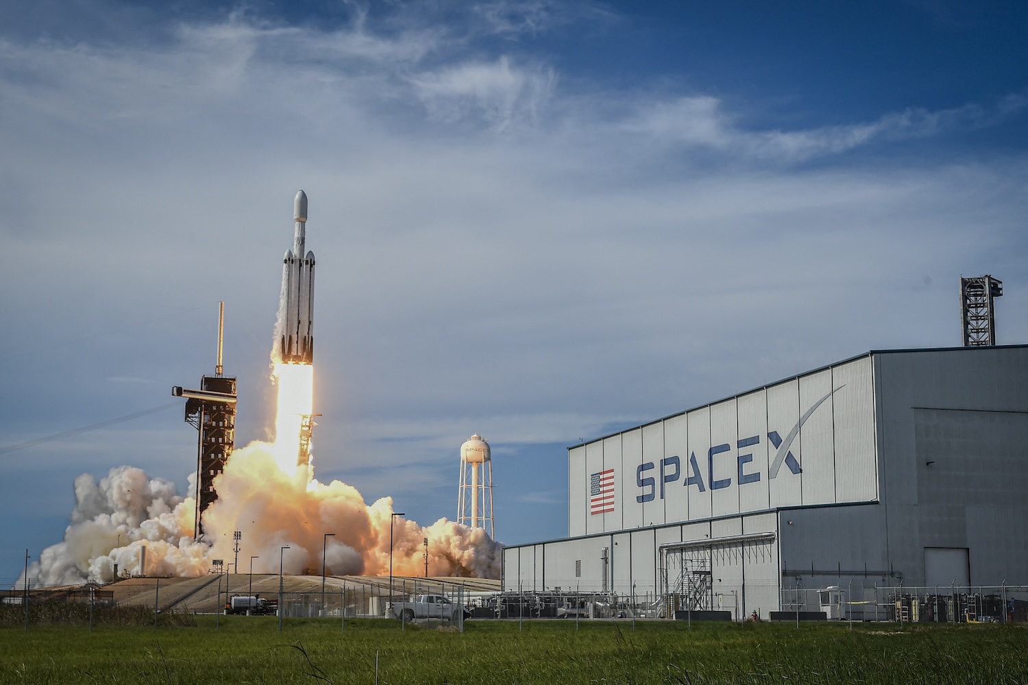 SpaceX rocket taking off from a launch site, in foreground SpaceX on a building.