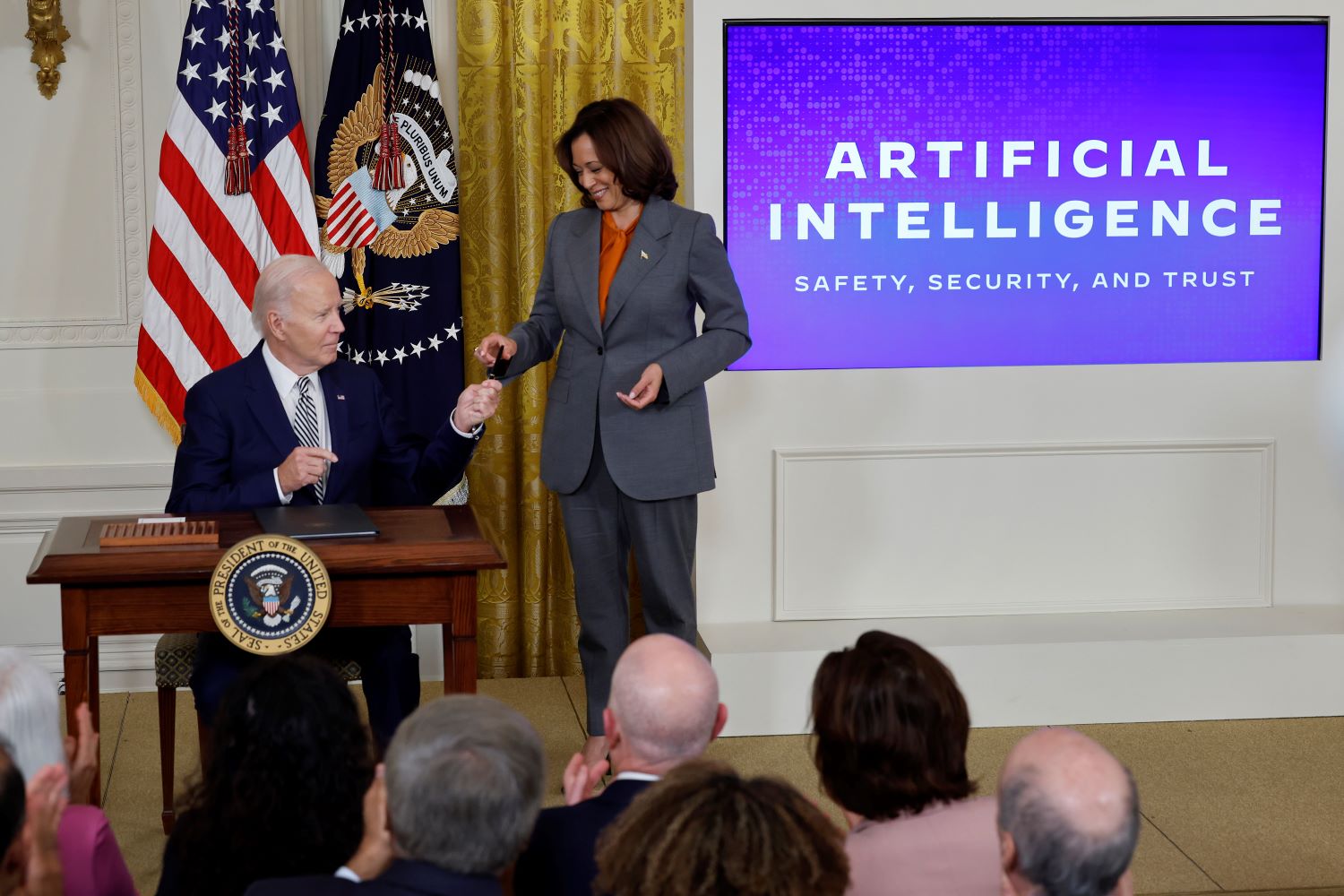 Vice President Kamala Harris hands president Joe Biden a pen to sign an executive order on artificial intelligence.