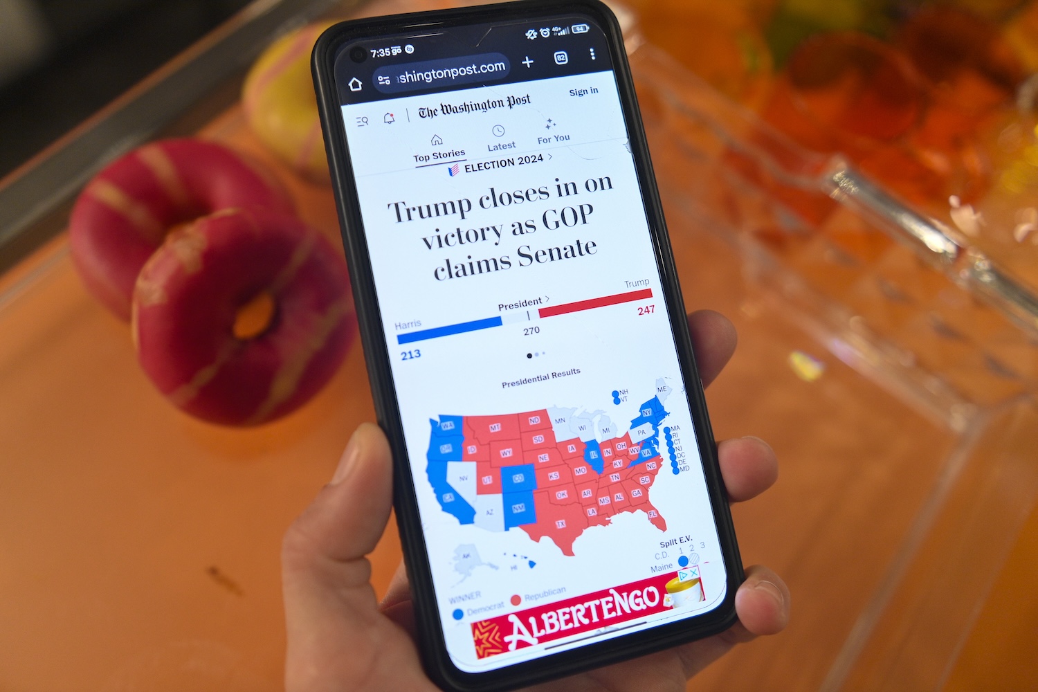 A phone in a man's hand showing a website tracking the 2024 U.S. presidential election.