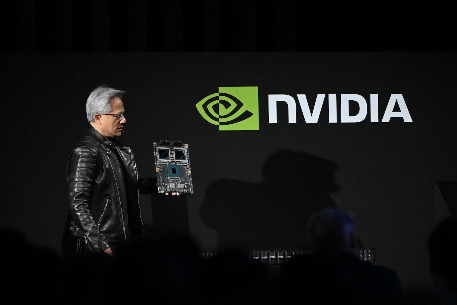 Jensen Huang, co-founder and CEO of Nvidia, holds up the company's AI accelerator chips for data centers on a black background with Nvidia logo.