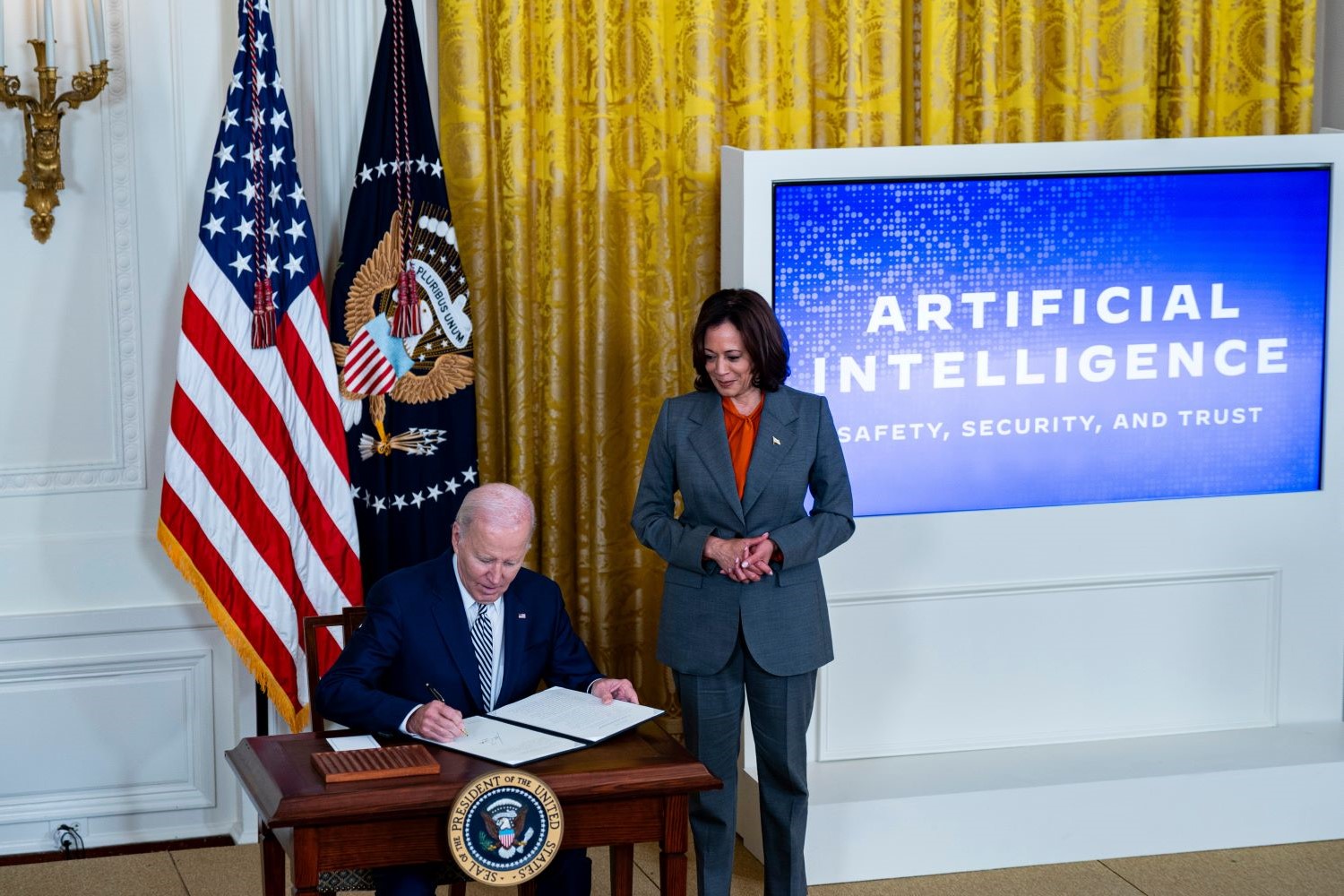 Kamala Harris stands over Joe Biden as he signs the 2023 AI executive order.