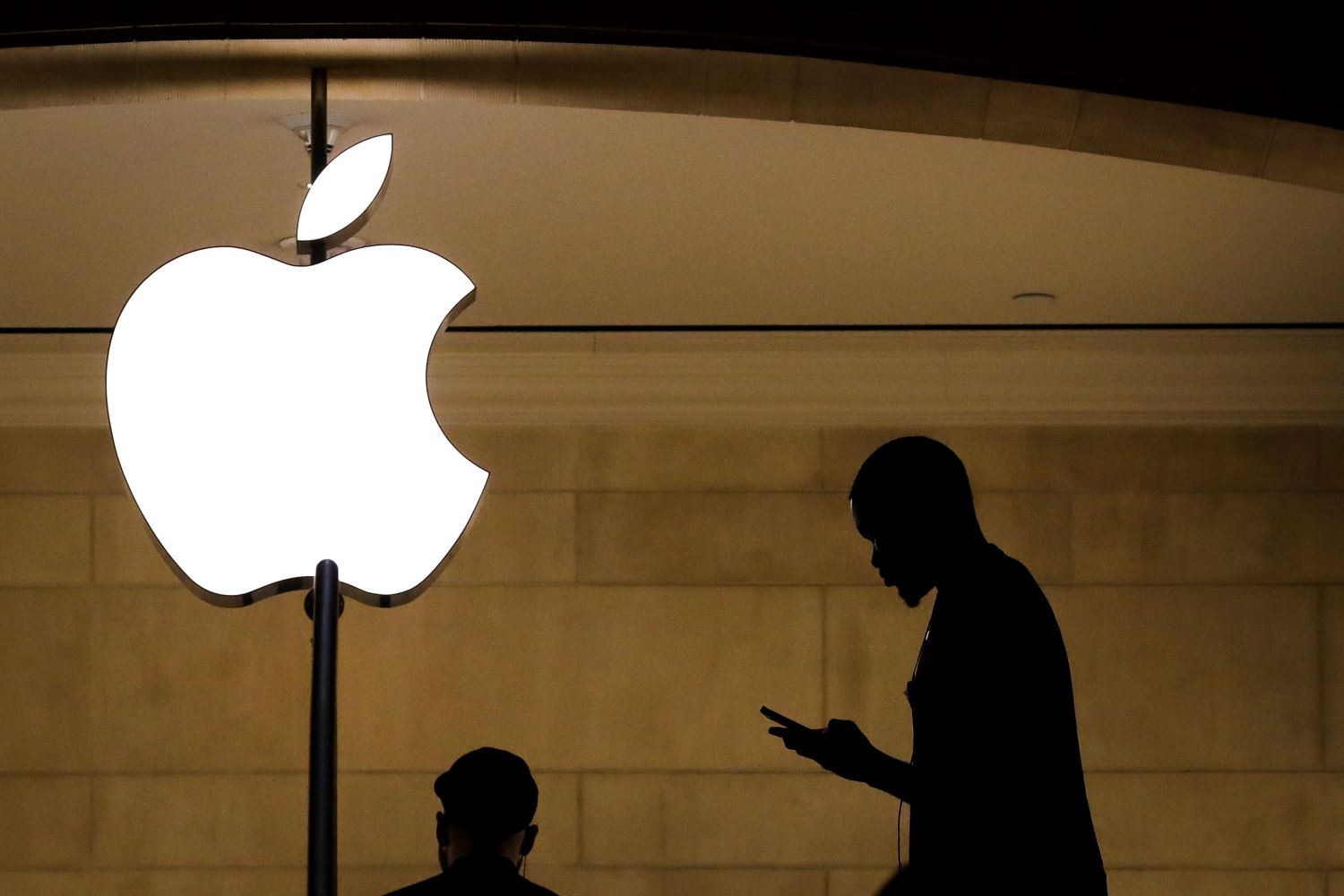 A silhouetted figure walks past the Apple logo.