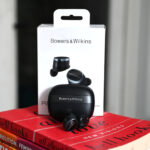 Shot of Bowers & Wilkins Pi8 earbuds with charging case and box on top of red book.