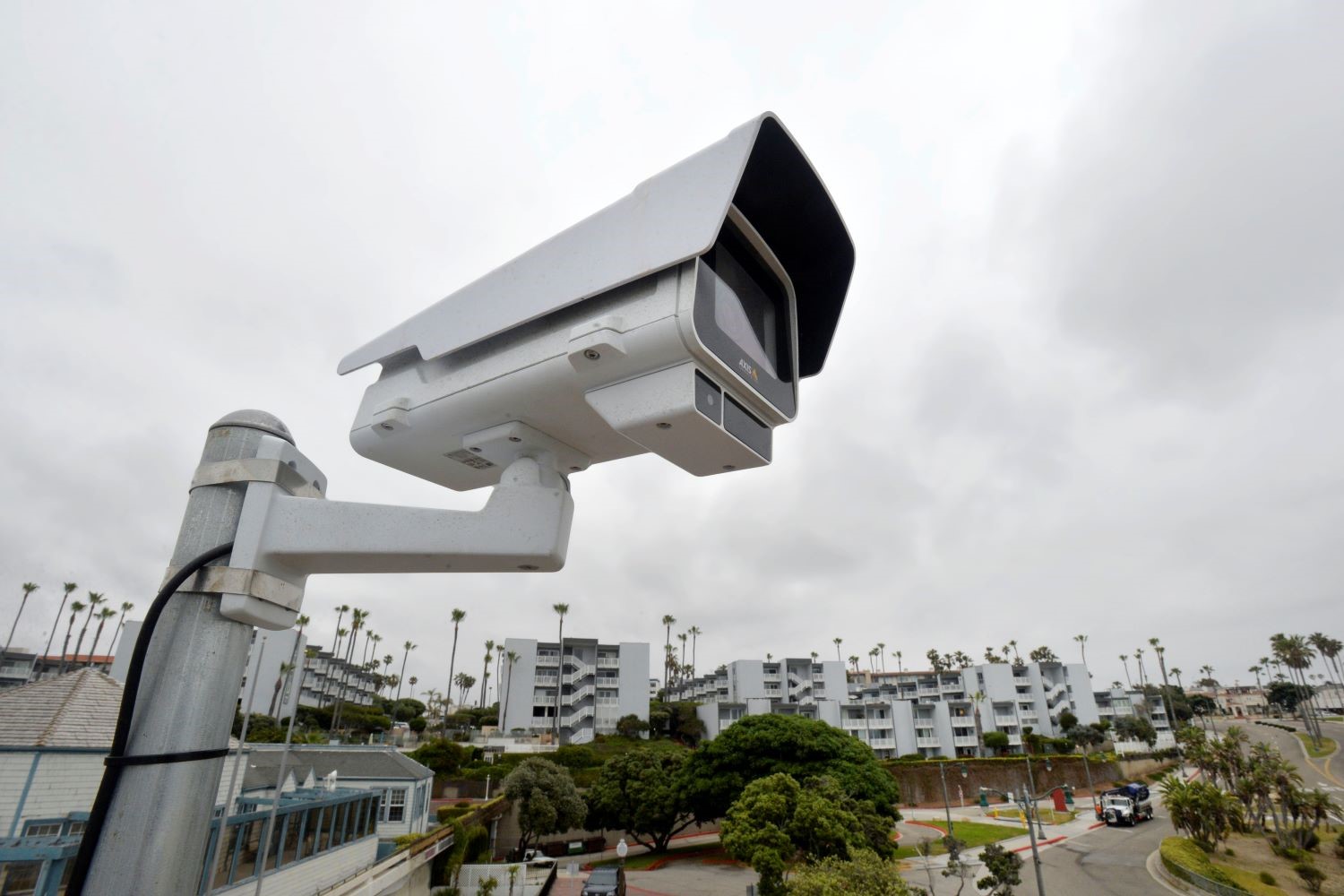 A large white surveillance camera in the foreground against apartment buildings far in the background.