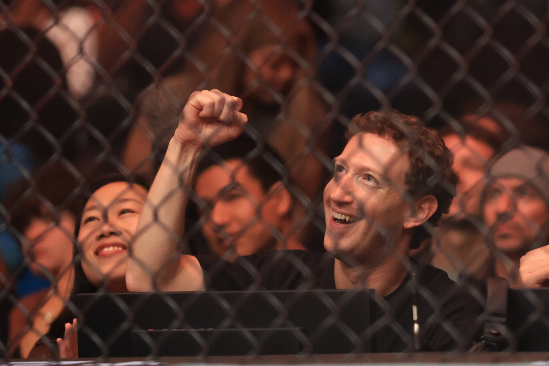 Mark Zuckerberg with his fist raised at a UFC event, taken from behind the cage