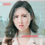 A woman's face overlayed with a graphic representation of an AI facial analysis template. A red label by her face says 'Angry'.