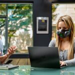 A person wearing a Razer Zephyr mask while typing on a laptop next to a person wearing a standard mask