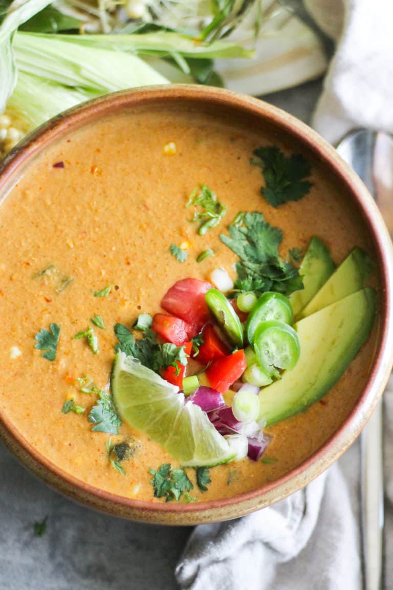 Vegan Corn Chowder in brown bowl with avocado, tomato and lime.