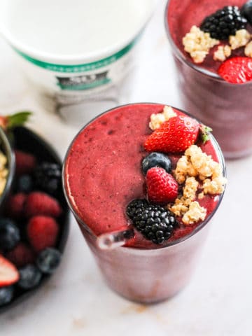 Berry Coconut Water Smoothie in a glass topped with fresh berries and granola with a tub of So Delicious yogurt alternative behind it.