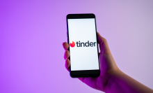 A person is holding a mobile phone with the Tinder dating app logo on its screen