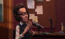 A stop-motion puppet of a man in a sweater and headphones in a recording booth.