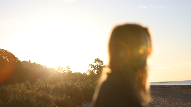 A still from the film, with a woman on the beach, her face obscured by the sun.