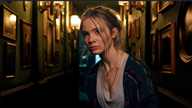 A woman looks concerned while walking down the gloomy corridor of a house.