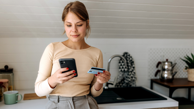 Person standing against counter in kitchen looking at gift card and smart phone