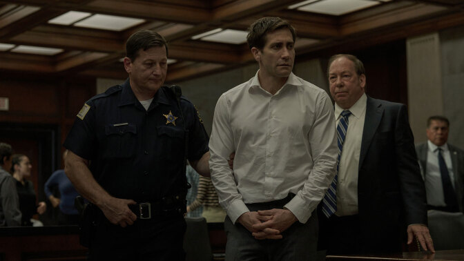 A man in a courtroom is led by a police officer.