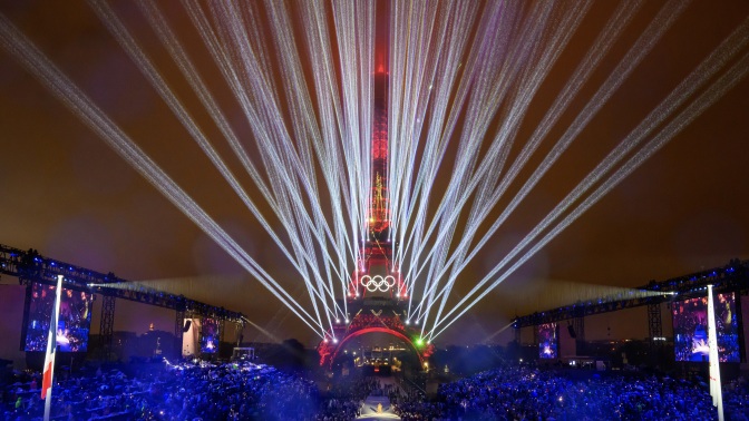 The Eiffel Tower lights up during a laser show at the opening ceremony of the 2024 Olympics;  the Olympic rings are suspended on its first level.