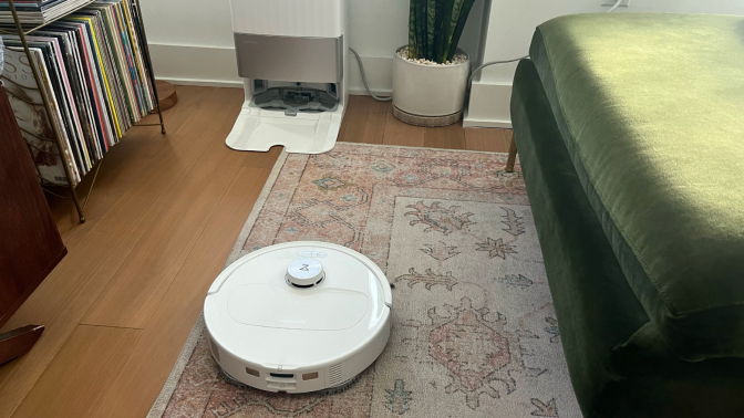 Roborock Qrevo Master robot vacuum cleaning rug with self-empty dock, record organizer, and green couch in peripherals