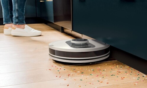 the shark ai robot vacuum cleans colorful sprinkles off a kitchen floor while someone wearing white slip-on shoes stands in the background